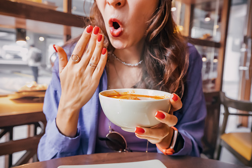 Girl tries a spicy and hot Tom Yam soup in a restaurant and reacts funny emotionally. Seasonings in the national cuisine and an unhealthy diet with overabundance of pepper