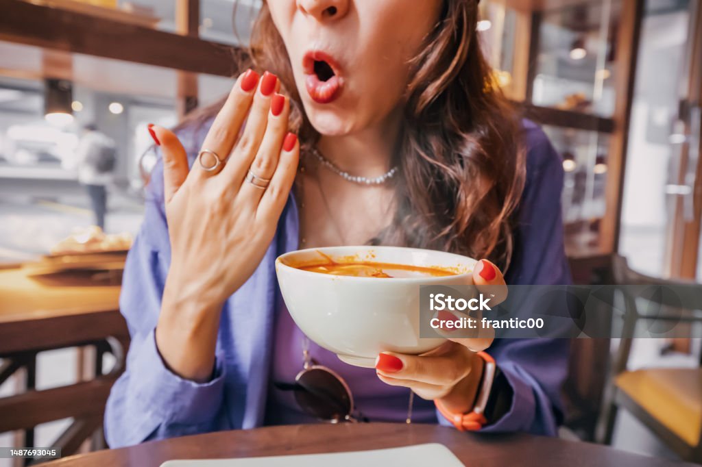 Girl tries a spicy and hot Tom Yam soup in a restaurant and reacts funny emotionally. Seasonings in the national cuisine and an unhealthy diet with overabundance of pepper Food Stock Photo