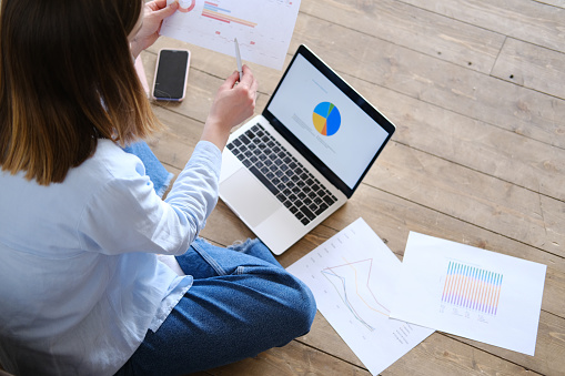 A young woman is studying or working remotely at home sitting on an armchair. Work from home office. The student uses distance learning on the computer and on the Internet. A young caucasian girl is working at a laptop in a relaxed atmosphere at home.