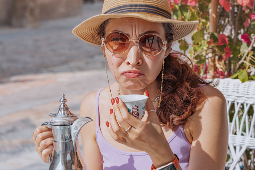 a disgruntled girl sniffs and tastes Arabic coffee