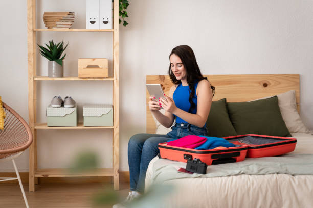 istock Woman sitting on her bed using digital tablet next to suitcase. 1487697745