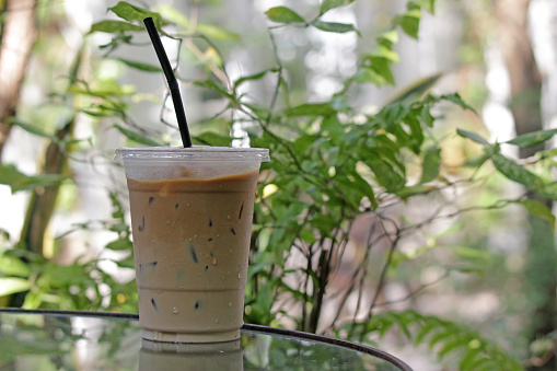 Refreshment concept, fresh cold iced coffee on a table in a tropical garden with sunlight and green foliage blurred in the background. No people.
