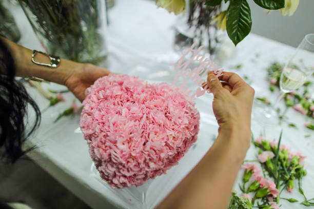 アジア人女性がフラワーアレンジメントのクラスを受講し、たくさんのカーネーションを使ってハート型の花束を作り、母の日を祝うために母親に贈っています。 - carnation mothers day florist flower ストックフォトと画像