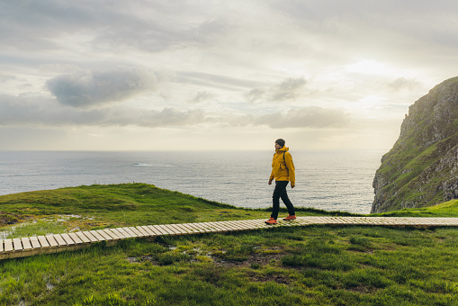 Side view of a male in yellow jacket contemplating the hiking trip on footpath with view of the ocean during sunset  in Scandinavia