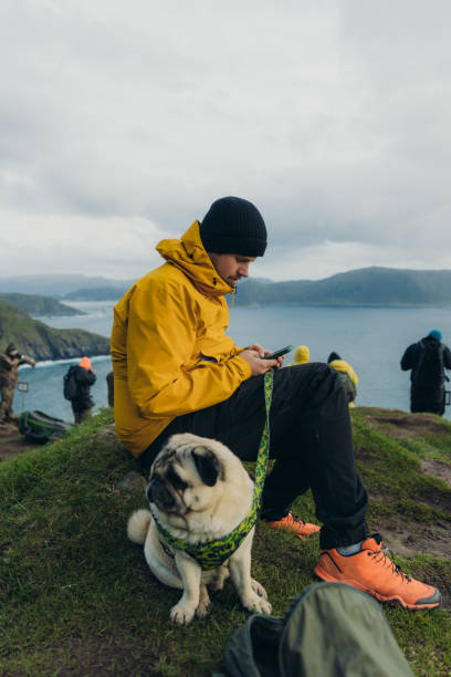istock Man with dog using smartphone on mountain top with sea view on Runde island, Norway 1487700447