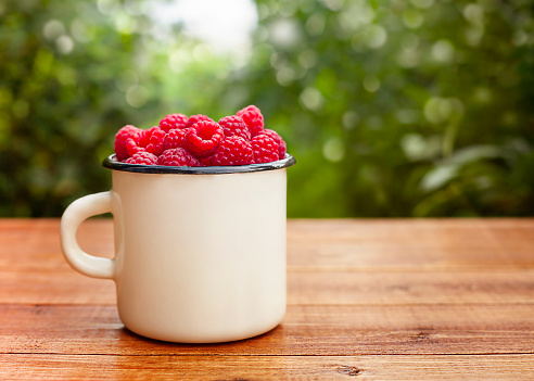 Raspberries in a cup on a wooden table in the garden close-up