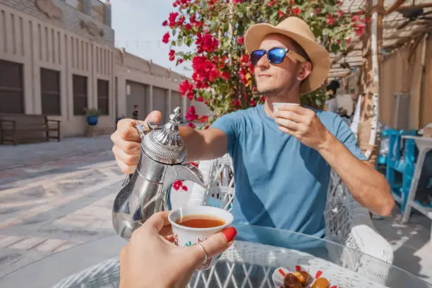Photo of As he takes a break from his travels in Dubai, a man finds respite in a traditional Arabic cafe, pouring a cup of aromatic coffee from a traditional dallah coffeepot.