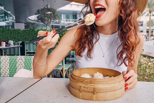 Girl with chopsticks eating delicious, traditional Chinese delicacy, Xiaolongbao dumplings, or baozi buns presented in a bamboo plate for an authentic touch.