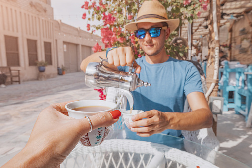 As he immerses himself in the vibrant culture of Dubai, a man indulges in the simple pleasure of pouring himself a cup of Arabic coffee from a traditional coffeepot in a charming cafe