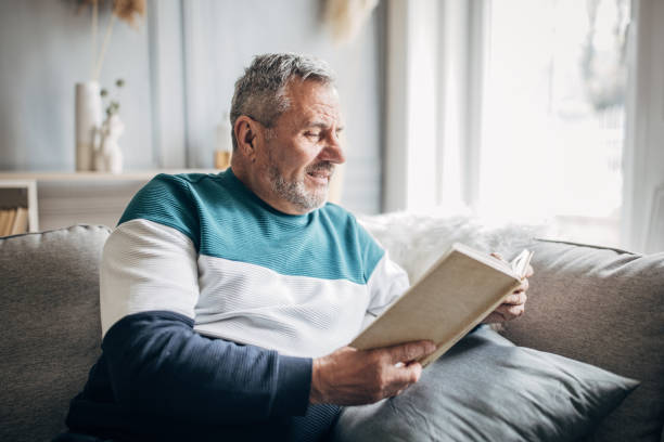 istock An elderly man is sitting on a sofa and reading a book at home 1487705896
