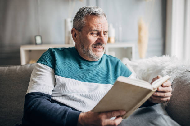 istock An elderly man is sitting on a sofa and reading a book at home 1487705932
