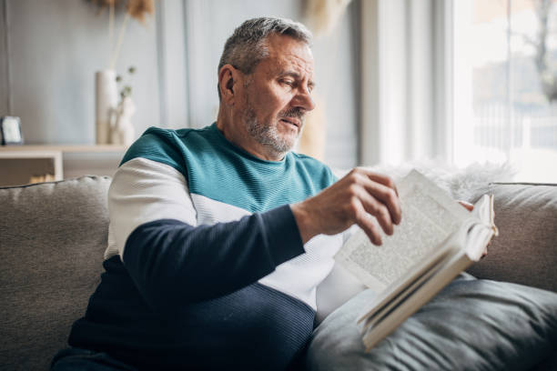 istock An elderly man is sitting on a sofa and reading a book at home 1487705967
