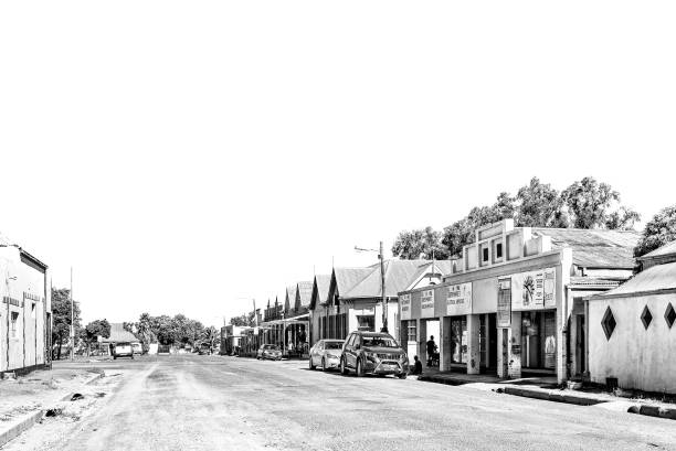 Jagersfontein, South Africa - Feb 21, 2022: A street scene, with historic buildings, people and vehicles, in Jagersfontein in the Free State Province. Monochrome