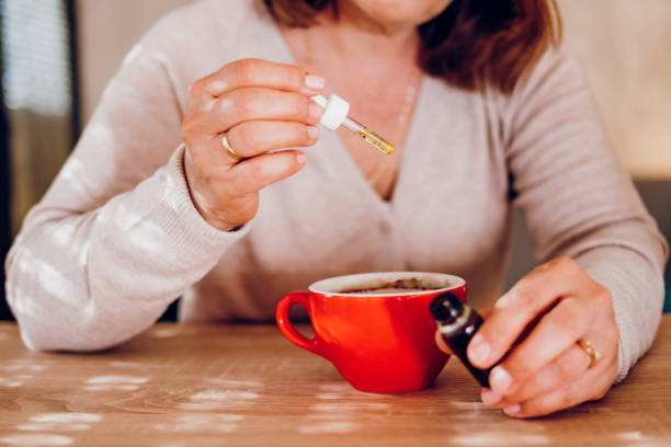 cbd óleo de cânhamo - mulher adicionando óleo de cannabis em uma xícara de chá - chinese medicine nutritional supplement herb pill - fotografias e filmes do acervo