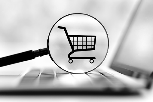 shopping cart on laptop computer, icon visible in magnifying glass. Web shop or shop concept for online shopping and home delivery