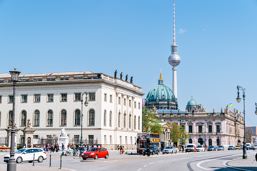 The photo captures Berlin's city center on a sunny day, with the iconic Fernsehturm and Berliner Dom in the background. The road is busy with cars, capturing the bustling energy of the city.