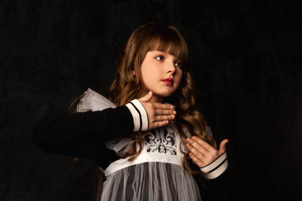 Portrait of cover girl in doll image gestured hands on black background, frozen pose looking away. Cute kid 9-10 year old with curly hair isolated in shadow. Theatrical show concept. Copy text space retrato de la chica de portada en imagen de muñeca con gestos con las manos sobre fondo negro, pose congelada mirando hacia otro lado. lindo niño de 9-10 años con cabello rizado aislado en sombra. concepto de espectáculo teatral. copiar espacio de text