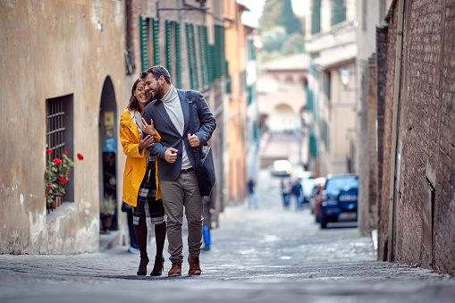 A young couple in love is enjoying emotional moments while walking the old city in a relaxed manner. Walk, rain, city, relationship