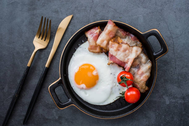 istock Fried eggs on a stylish ceramic plate with handles with fried bacon and cherry tomatoes on a dark background. Breakfast, lunch and dinner. Delicious food. Cooking. 1487717991