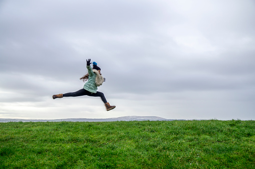 Ten year old girl winter countryside portraits. Running leap on grassy hill,