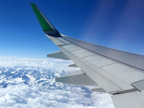 Big aircraft wing high up over the wide snowy mountains range. Air transportation. Travel destinations. Skyline in the atmosphere