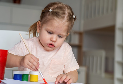Girl draws a children's drawing with paints and a brush.