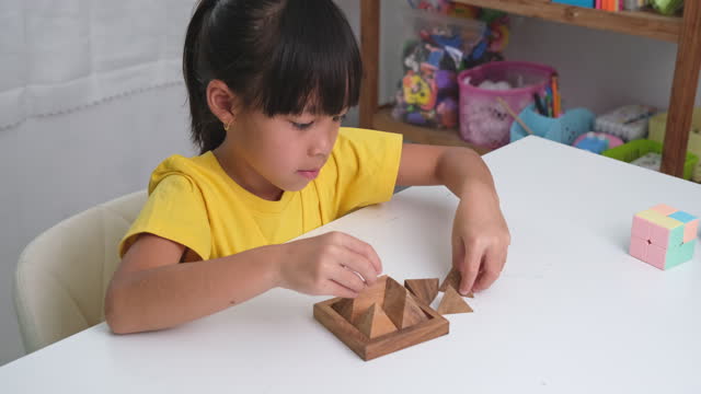 Asian cute little girl playing with wooden toy jigsaw puzzle pyramid on table. Healthy children training memory and thinking. Wooden puzzles are games that increase intelligence for children.