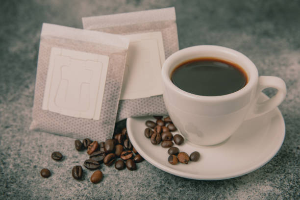 istock Drip coffee bags, coffee beans and a white cup on a texture table. Ground coffee for brewing in a cup, paper bag drip coffee filter packaging. Place to copy. Place for text. 1487730700