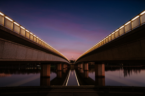 A colourful cityscape of Commonwealth Avenue bridge over Lake Burley Griffin in Canberra looking towards Parliament House at sunset