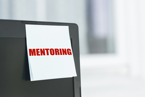 The word mentoring written on a white sheet of paper sticked to laptop monitor.