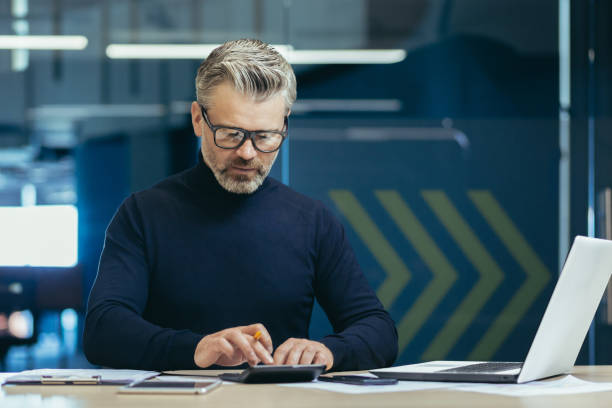 istock Serious thinking financier business analyst working with documents inside office, mature adult accountant on paper work calculating with calculator and laptop inside office 1487736002