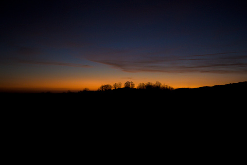 silhouette of trees on hill at sunset with sky in soft colors in magenta, pink, blue horizontally