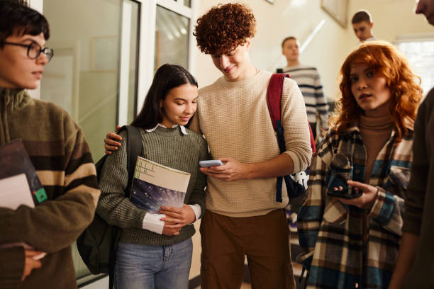 istock Smiling high school couple using cell phone in a hallway. 1487737917