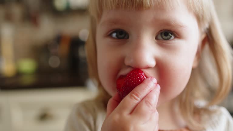 Little girl eats fresh strawberry for breakfast at home in the morning