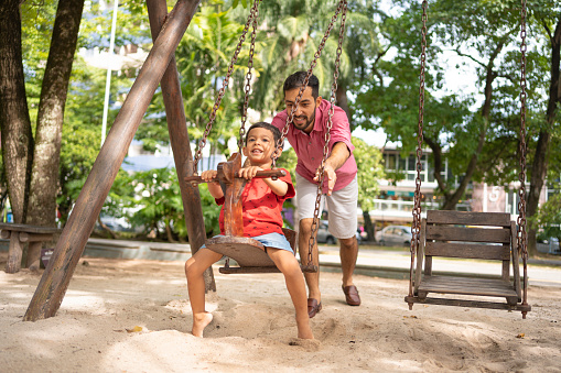 Father pushing son on swing in park