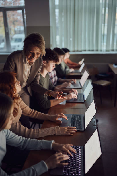 istock Happy mature professor assisting students in e-learning over computers at high school. 1487738851