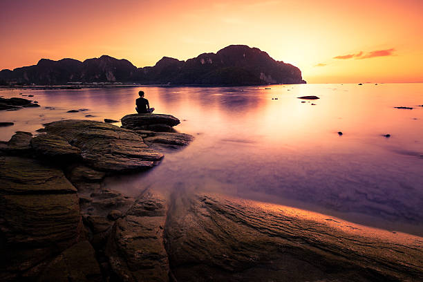 Praying on the rock Man sitting in loto position on a rock of Phi Phi island, Thailand. silhouette lounge stock pictures, royalty-free photos & images