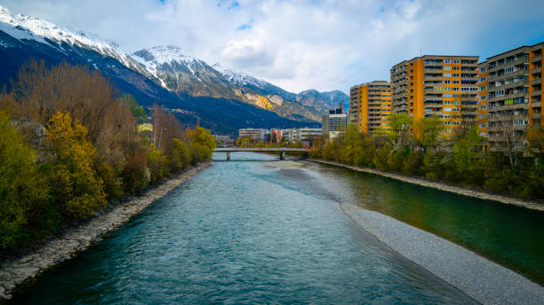 Alps Mountains Northern Range landscape at sunrise, snow-covered peak skyline and cloudscape over the Inn River, colorful forest, and town buildings in western Austria, train travel scenery photo