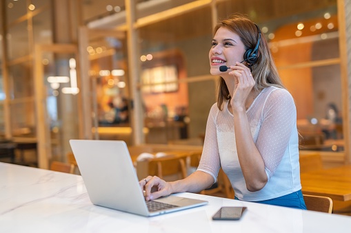 Half length mid shot of multiracial customer support woman working out of home, from a workspace shared office cafe.