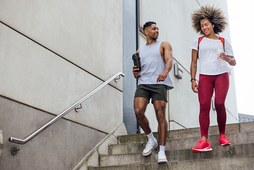 A shot of two friends, one male and one female, walking to the gym together in Newcastle Upon Tyne, North East England. They are both smiling and talking, dressed in activewear and carrying reusable water bottles.
