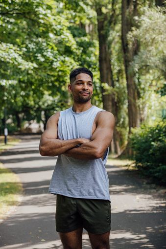 A shot of a multiracial male with a natural green backdrop in a park in Newcastle Upon Tyne, North East England. He is wearing activewear, has his arms crossed and is looking away from the camera, with a proud smile.