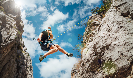 Low angle view of a female climber with safety harness climbing on artificial rock wall outdoors.