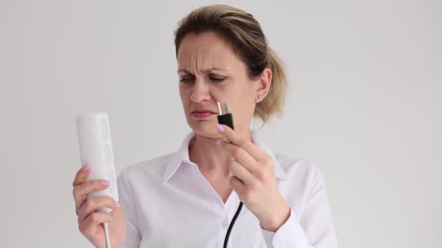 Woman confused by wrong plug and socket near white wall