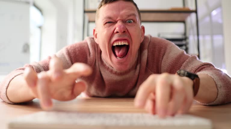 Grimacing internet fraud guy types on PC keyboard at table