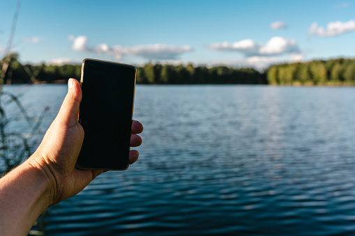A male tourist uses the phone on the shore of the lake on a beautiful sunny day.