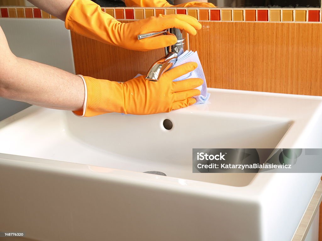 Faucet cleaning Hands in gloves with rubber cleaning bath faucet Bathroom Stock Photo