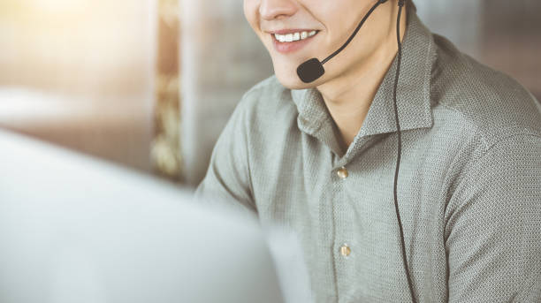 istock Young man with headsets is talking to a client, while sitting in modern sunny office. Call center operators at work 1487763599