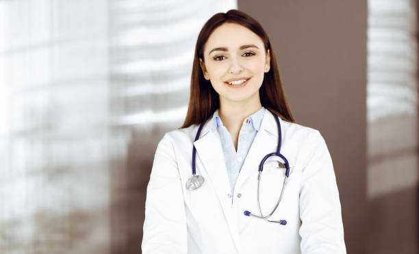 une jeune femme-médecin souriante se tient dans le bureau d’une clinique. portrait d’une femme médecin sympathique. service médical parfait dans un hôpital. concept de médecine - portrait doctor paramedic professional occupation photos et images de collection