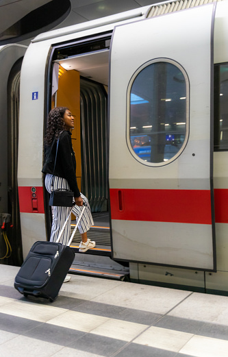 Wide shot of businesswoman being late and rushing to to catch the train that is about to depart any second. She is running and dragging her suitcase.