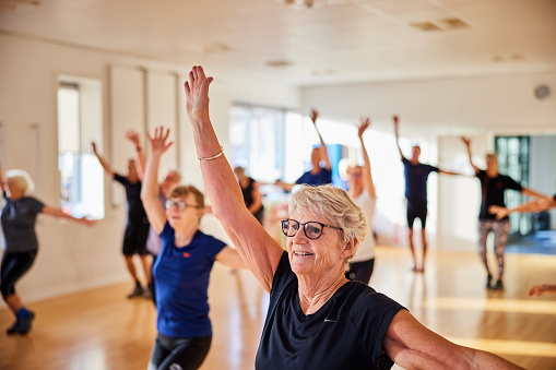 Smiling senior woman in sportswear doing an aerobics exercise class with other seniors in a health club